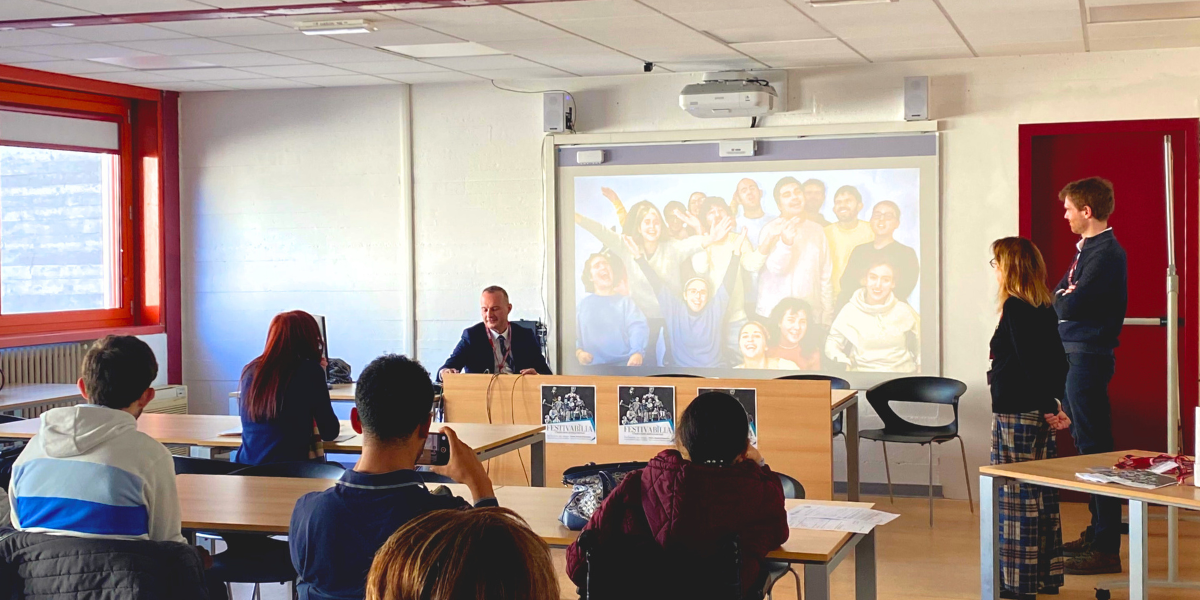 Massimo Salgaro presenta il gruppo studentesco Teatro a rotelle durante la giornata di studi Inclusion on Stage, con pubblico sullo sfondo, Nicoletta Vicentini e Manuel Boschiero in piedi a lato della cattedra.