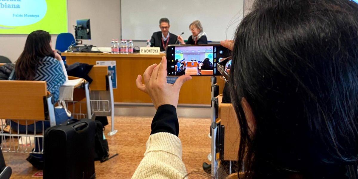 Pablo Montoya in cattedra per la conferenza "desde los margenes" viene fotografato da una partecipante alla conferenza. Pubblico sullo sfondo.